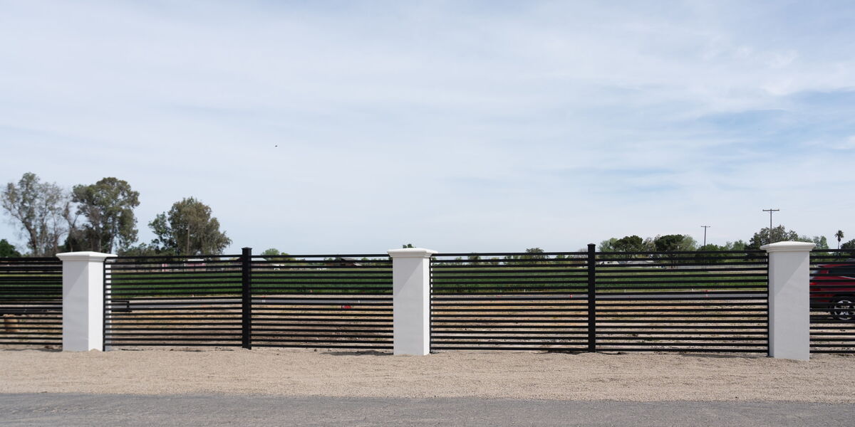 Black horizontal-slat metal fence with white stucco pillars along a Sacramento property line