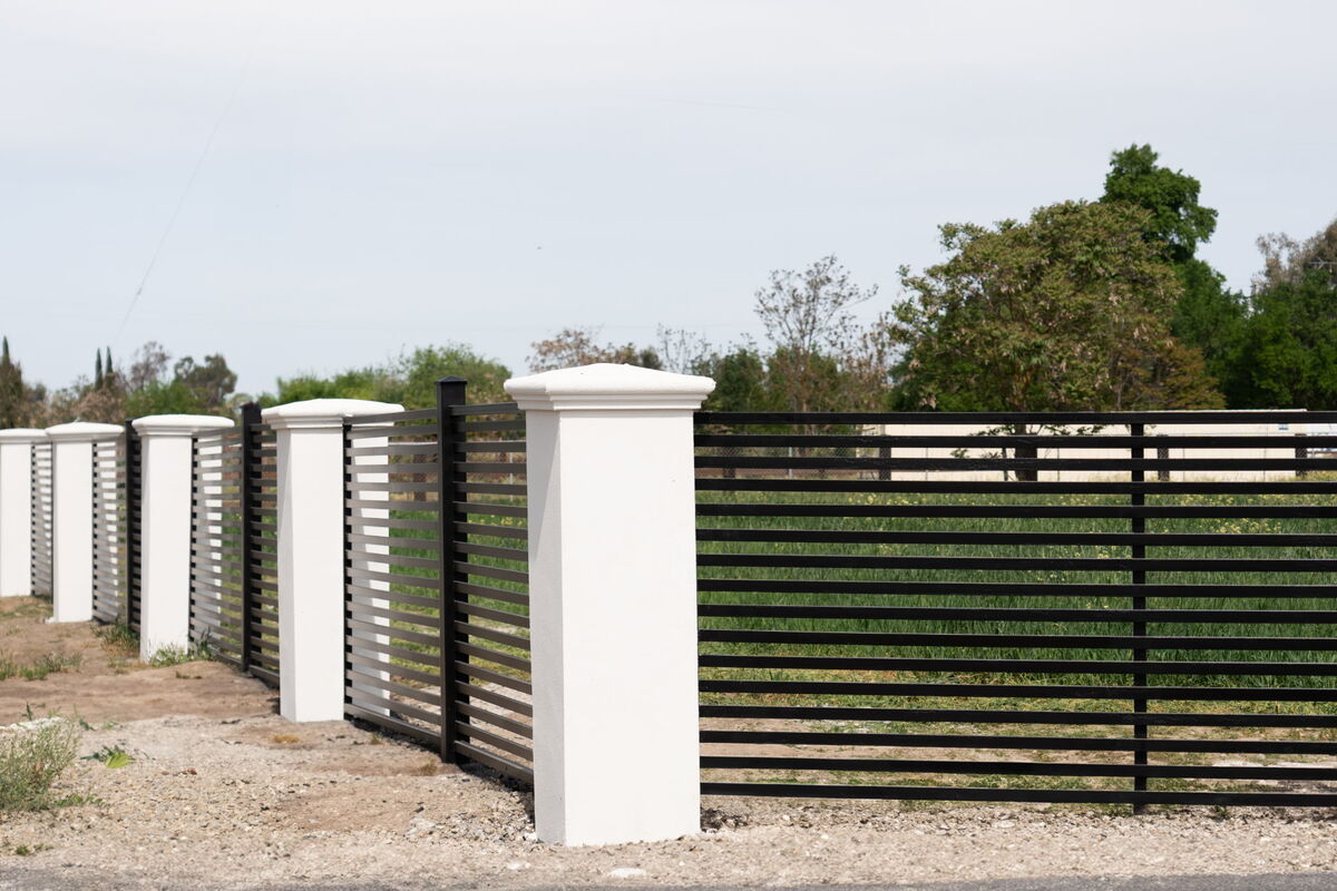 Corner run of black metal slat fencing between white stucco columns